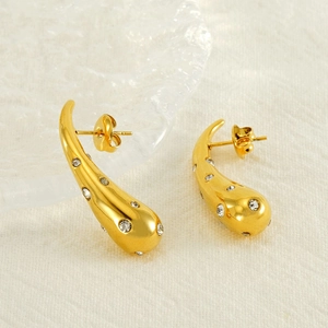 Golden teardrop earrings with shimmering crystals on a soft beige fabric background