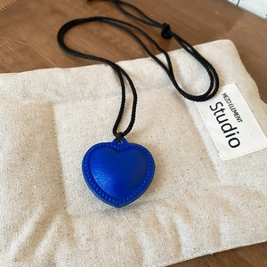 Detailed shot of blue textured heart pendant with black braided cord on a soft canvas mat