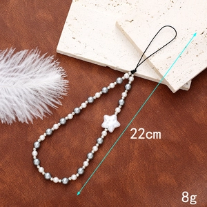 Detailed view of handmade beaded phone strap with white stars and pearls on a stone stand
