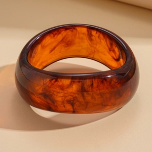 Macro shot of thick amber acrylic bangle showing tortoiseshell texture and polished finish
