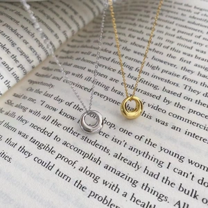 Colliers à pendentifs anneaux dorés et argentés minimalistes sur fond de livre ancien