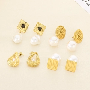 Flat lay of gold spiral earrings and Evil Eye square studs with white pearls