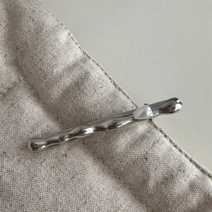 Close-up of a silver wave-shaped metal hair clip featuring a white pearl on linen fabric