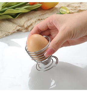 Close-up of a hand placing a brown egg into a spiral stainless steel spring holder
