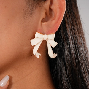 Close-up of a cream bow earring with gold edges worn by a model in soft lighting