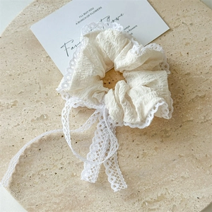 Detailed shot of white seersucker hair scrunchie with lace trim and long ribbon bow