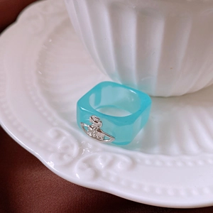 Detail of light blue resin ring with silver planet emblem on vintage white ceramic plate