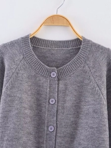 Detailed view of the gray knitted cardigan featuring round neck and purple buttons