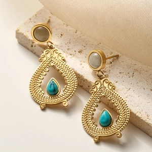 Retro gold teardrop earrings with turquoise stones and white studs on a stone surface