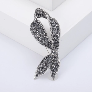 Elegant silver ribbon brooch adorned with black rhinestones on white studio pedestal
