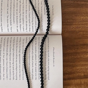 Minimalist black onyx beaded necklace displayed on an open book over a dark wood desk