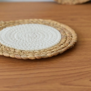 Close-up of a handmade round straw and cotton woven heat-resistant table mat on wood