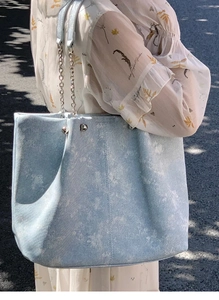 Detail of light blue washed denim tote bag with silver chain strap worn outdoors