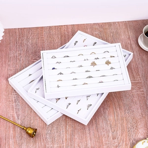 White jewelry display tray with multiple ring slots on a wooden table setup