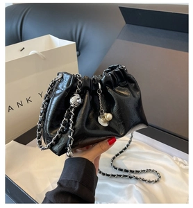 Detail of black pleated cloud bag with silver chain and pearl charm on silk and gift box