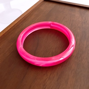 Detailed view of pink marble resin bangle on a dark walnut tray with polished finish