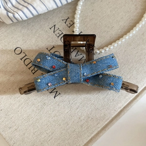 Detailed close-up of blue denim bow hair claw clip with colorful rhinestones on a book