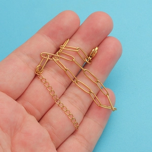 Gold paperclip chain bracelet with lobster clasp held against a soft blue background