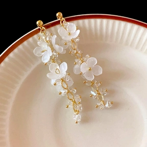 Détail de boucles d'oreilles fleur mate blanche avec chaîne dorée et perles de cristal clairs
