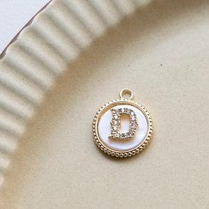 Detailed view of a gold-plated circular shell pendant featuring a zircon letter D inlay
