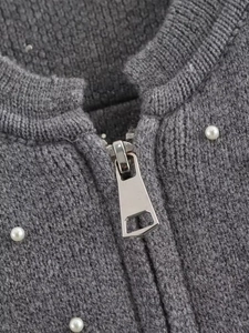 Detailed view of pearl embellishments and silver zipper on a gray knit bomber jacket