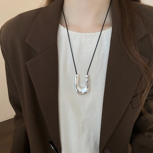 Close-up of irregular silver U-shaped pendant on black cord worn over professional attire