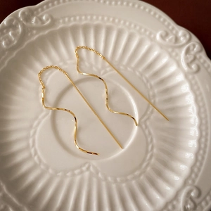 Detailed view of elegant gold wavy tassel drop earrings resting on a white vintage ceramic plate