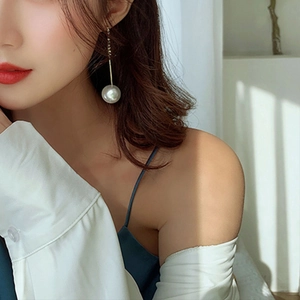 Detail of elegant gold drop earring with a large white pearl worn by a female model