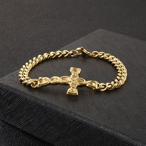 Macro shot of gold Cuban link bracelet featuring a central cross charm and lobster clasp