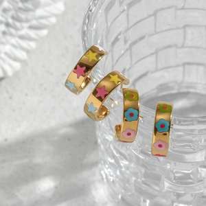Detail of gold earrings with colorful enamel star and flower patterns on textured glass