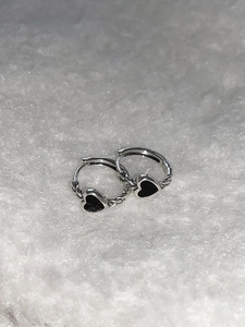 Close-up of twisted silver hoop earrings with black heart charms on white faux fur