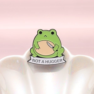 Funny green frog enamel pin holding a knife with Not a Hugger text banner