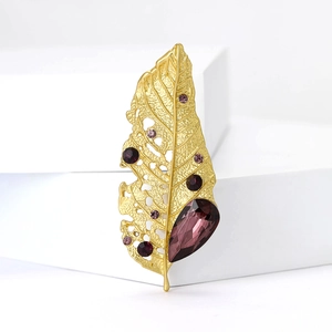 Golden leaf brooch with purple teardrop gemstones and crystals on white background