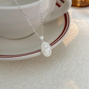 925 sterling silver heart shell necklace featuring an oval pendant on a white ceramic cup