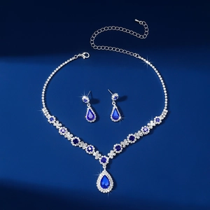 Elegant silver necklace and teardrop earrings set with deep blue crystals on blue surface