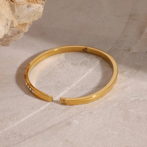 Gold plated stainless steel hinged bangle with cubic zirconia on marble surface