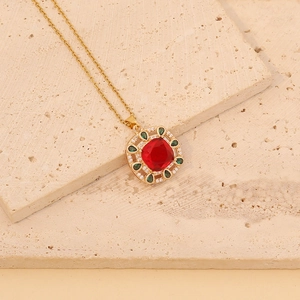 Detailed close-up of a vintage golden necklace with a red gem and green accents