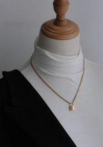 Detail of a minimalist gold padlock pendant necklace on a black and white business outfit