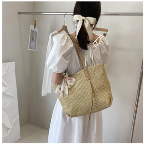 Detail of large straw tote bag featuring woven texture and decorative silk scarf accent