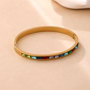Gold stainless steel bangle with rectangle rainbow gemstones on a beige background