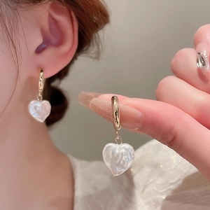 Dettaglio di orecchini di perle a forma di cuore con eleganti ganci a C in finitura oro