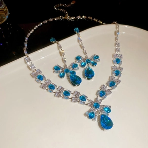 Detail of silver jewelry set with blue waterdrop zircon and bowknot on a white plate
