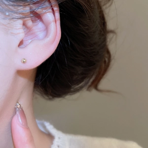 Detailed close-up of a minimalist small gold ball stud earring on a human earlobe