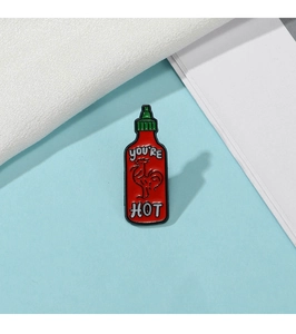 Detail of red chili sauce enamel pin featuring You're Hot text on blue surface