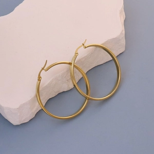 Detail shot of oversized gold flat hoop earrings resting on a textured white stone