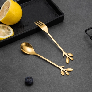 Detail of golden leaf-shaped handle on stainless steel dessert spoon and fruit fork