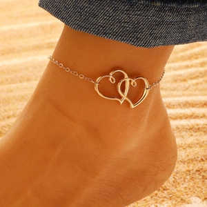 Close-up of golden interlocking heart anklet on ankle with beach background