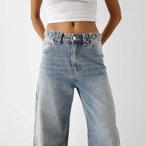 Détail d'un jean large bleu clair à taille haute montrant la coupe à la taille et aux hanches