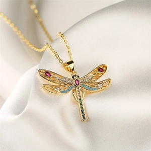 Macro shot of gold dragonfly pendant with colorful zircon stones on white silk fabric