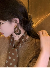 Detail of dark resin hollow drop earrings worn with a silk scarf in a vintage setting